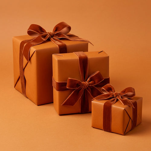 Three burnt orange solid color wrapping paper gift boxes with ribbons on an orange background