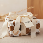 Modern abstract dot wrapping paper with brown, tan, and cream circles, tied with an elegant cream satin ribbon and gift tag.