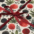 Christmas wrapping paper with a festive red, green, and black botanical pattern, tied with a deep red satin ribbon.