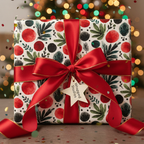 Holiday wrapping paper with red and green modern foliage design, a red satin bow, star tag, and festive lights in the background.