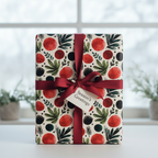 Christmas wrapping paper with red berries, green leaves, and black dots, tied with a deep red satin ribbon and "Season's Greetings" tag.