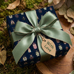 Square gift wrapped in modern beetle-print wrapping paper with a sage green ribbon and "With Love" tag.
