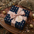 Square birthday gift wrapped in dark blue paper with a colorful bug pattern and pink ribbon bow.