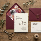 Elegant burgundy wedding invitation card with floral envelope liner on wood table by Wrapped Studios.