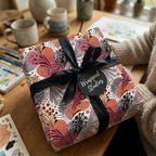 Luxury boho floral wrapping paper in pink and terracotta on a gift box with black ribbon by Wrapped Studios.