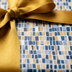 Luxury gift wrap by Wrapped Studios featuring a modern blue and gold geometric pattern tied with a satin gold ribbon.