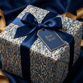 Luxury gift box in navy and gold mosaic wrapping paper, tied with a satin ribbon and a "For You" tag by Wrapped Studios.