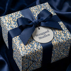 Luxury gift box wrapped in navy and gold mosaic paper with a navy ribbon bow, by Wrapped Studios.