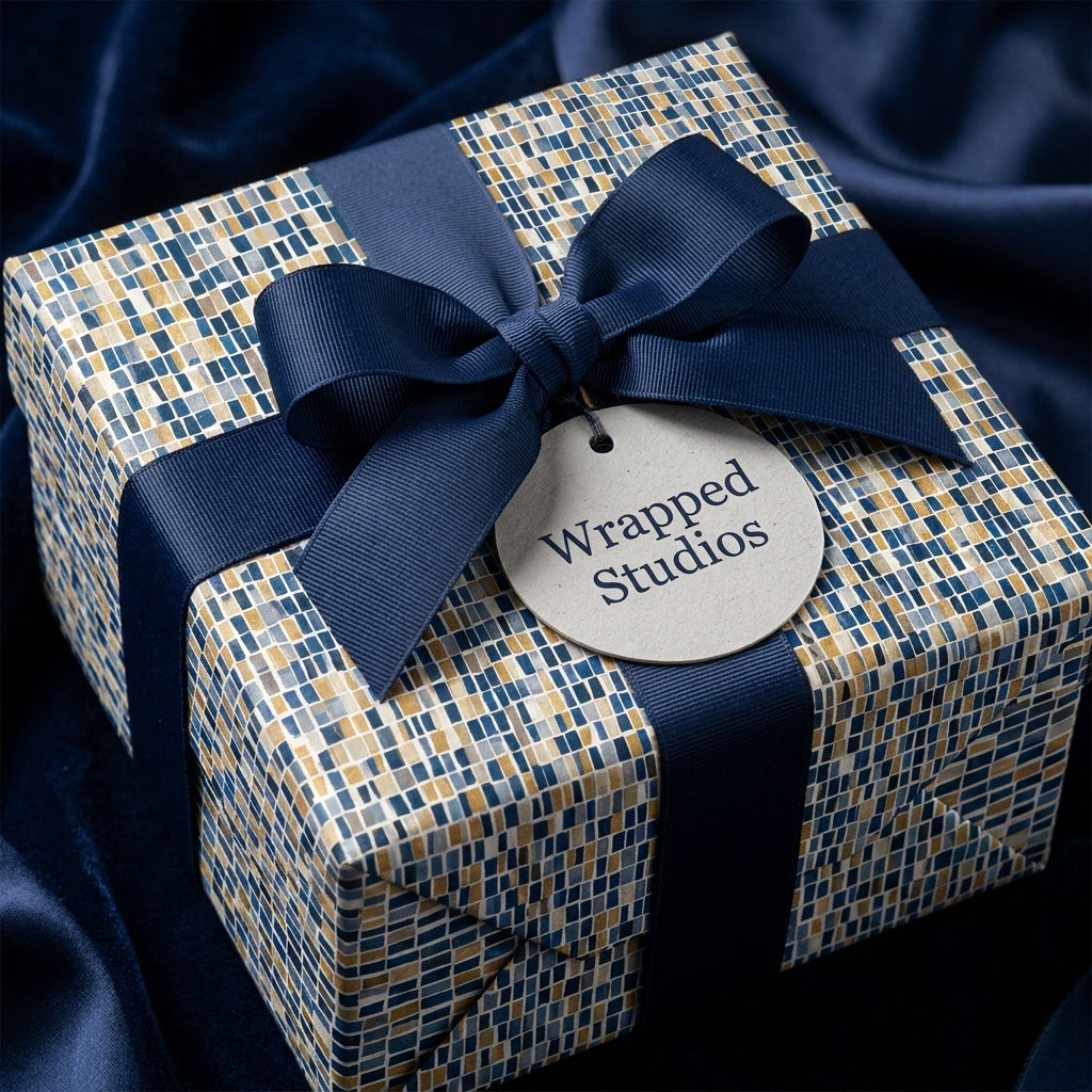 Luxury gift box wrapped in navy and gold mosaic paper with a navy ribbon bow, by Wrapped Studios.