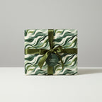 Gift box in modern wave-patterned wrapping paper, tied with an olive green ribbon, from Wrapped Studios.