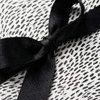 Minimalist black and white wrapping paper with a dash pattern and black satin bow by Wrapped Studios.