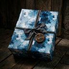 Blue abstract wrapping paper by Wrapped Studios on a gift box with a grey ribbon and wooden Cheers tag.