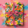 Colorful gift wrapped in modern abstract pattern paper, with pink ribbon and "A Burst of Joy!" tag.