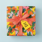 Square gift wrapped in colorful abstract wrapping paper with a coral ribbon and "For the best!" tag.
