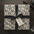 Modern abstract wrapping paper with organic black and beige patterns, tied with a black velvet ribbon and gift tag, on a dark wood table.