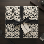 Modern abstract wrapping paper with organic black and beige patterns, tied with a black velvet ribbon and gift tag, on a dark wood table.