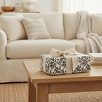 Modern black and white abstract wrapping paper with a cream ribbon and bow on a rustic wooden coffee table.