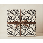 Modern abstract wrapping paper with black, grey, and cream organic shapes, tied with a luxurious brown satin ribbon.