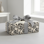 Modern abstract wrapping paper with a beige, black, and white pattern, tied with a chic gray ribbon and bow, perfect for unique gift wrap.