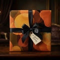 Modern abstract art wrapping paper with warm orange, brown, and black circles, tied with a black satin bow and "A Special Delivery" tag, on a dark wood table in an elegant interior.