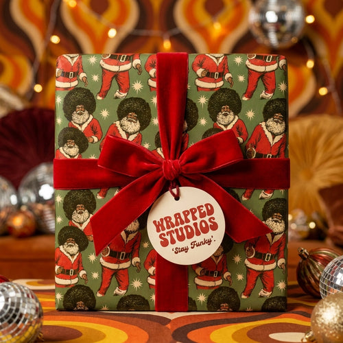 Funky Black Santa wrapping paper by Wrapped Studios with red velvet bow in retro 70s holiday setting.