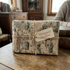 Vintage map wrapping paper tied with rustic twine and a Wrapped Studios gift tag on a wooden table.