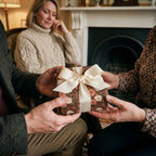 Hands holding a luxury gift in vintage floral wrapping paper with cream bow, by Wrapped Studios.