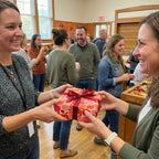 Two women exchange a gift in autumn apple wrapping paper with red ribbon, by Wrapped Studios.