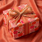 Apple wrapping paper with pink and orange fruit on a gift box with a raffia bow by Wrapped Studios.