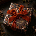 Dark gothic floral wrapping paper with a rust velvet bow on a gift box by Wrapped Studios.