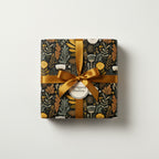 Square gift wrapped in black floral wrapping paper with a gold ribbon and bow.