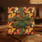 Elegant gift wrapped in autumnal leaf print wrapping paper with a dark green ribbon and bow.