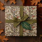 Elegant gift wrapped in vintage floral wrapping paper with green ribbon on a wood table with fall leaves.