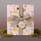 Gift box wrapped in pink floral wrapping paper with a neutral bow and leaf tag for autumn celebrations.