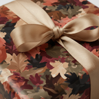 Close-up of a gift wrapped in autumnal leaf wrapping paper with a gold satin ribbon and bow.