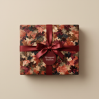 Elegant autumn leaf wrapping paper with a deep red ribbon and bow on a square gift box.