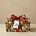 Gift wrapped in modern tree-patterned wrapping paper with a rust-colored ribbon bow and tag.