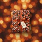 Gift wrapped in autumn leaf floral wrapping paper with copper satin ribbon and tag, festive bokeh background.