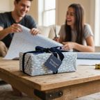 Young couple wrapping gifts with elegant blue patterned wrapping paper and navy velvet ribbon.