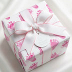 Square gift wrapped in baby shower wrapping paper with pink footprints and a white ribbon.