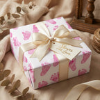 Gift wrapped in baby shower wrapping paper with pink footprints and a gold ribbon.
