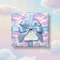Pastel camo wrapping paper on a square gift box, with a blue satin bow and "A little something sweet!" tag.