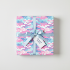 Square gift wrapped in pastel camo wrapping paper with a light blue satin ribbon and a white gift tag.