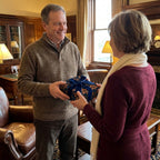 Man gifting a present in luxury wrapping paper with navy floral pattern and velvet bow, by Wrapped Studios.