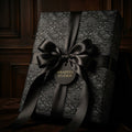Luxury black wrapping paper with elegant gothic floral pattern and black satin bow by Wrapped Studios.