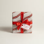 Gift box wrapped in baseball-themed paper, finished with a red satin ribbon and "Wrapped Studios" tag.
