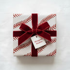 Square gift wrapped in baseball stitch wrapping paper with a velvet ribbon and bow.