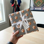 Grey baseball wrapping paper on a sports gift box with a white ribbon bow, by Wrapped Studios.