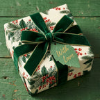 Luxury Christmas gift wrap with holly pattern, green velvet ribbon, and leaf tag. Wrapped Studios.