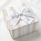 Beige striped wrapping paper with white bow and Joy tag, elegant luxury gift wrap by Wrapped Studios.